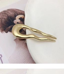 Close-up of golden wavy U-shaped metal hairpin on white plate highlighting its smooth finish
