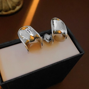 Close-up of irregular C-shaped silver metal earrings with a high-polished glossy finish