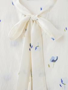 Detail view of the elegant bow-tie collar on white blouse with blue floral prints