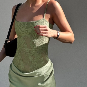 Close-up of sage green lace camisole top featuring intricate floral texture and slim straps