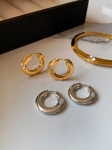 Detail of gold and silver hoop earrings with inlaid cubic zirconia on marble background