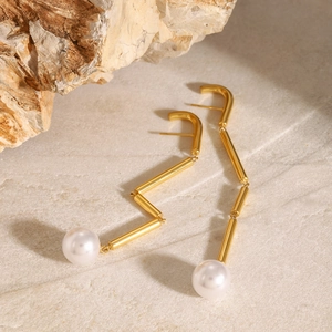 Detail of gold tassel earrings with pearls set against natural stone for a luxury feel
