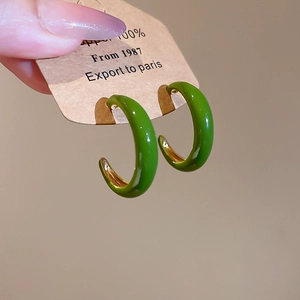 Elegant dark green and gold C-shaped enamel hoop earrings held on a display card