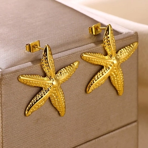 Elegant gold starfish stud earrings displayed on a brown textured jewelry box edge