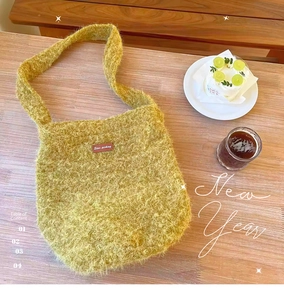 Detail der weichen senfgelben Plüsch-Schultertasche mit Lederetikett auf dem Schreibtisch
