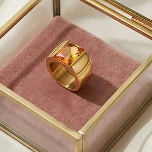 Macro shot of gold-plated wide band ring featuring a square orange gemstone in a gift box
