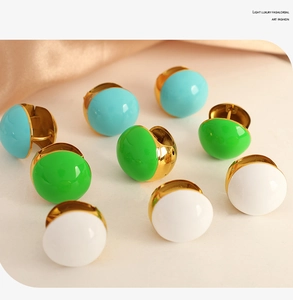 Detail view of round enamel huggie earrings in blue green and white with gold base