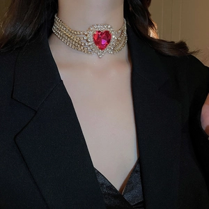 Detail of a multi-layer gold choker with a vibrant red heart-shaped gemstone pendant