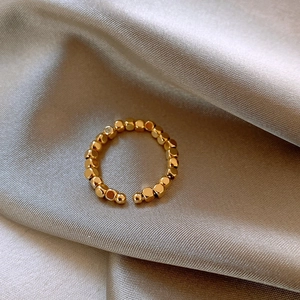 Dettaglio anello aperto placcato oro 14k con perline quadrate su tessuto di seta