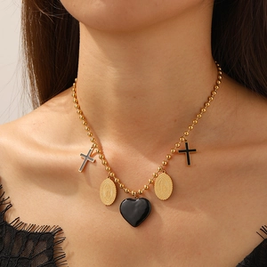 Golden beaded necklace with black cross, oval medal, and heart charms on a female model
