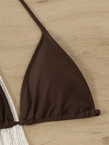 Detail of dark brown bikini top with ruched hem and white lace trim on wood background