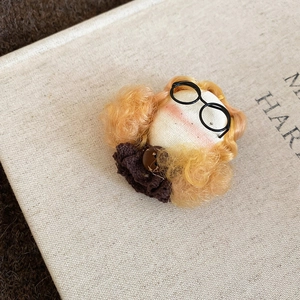 Close-up of a flocking doll brooch with golden curls and glasses on a linen texture