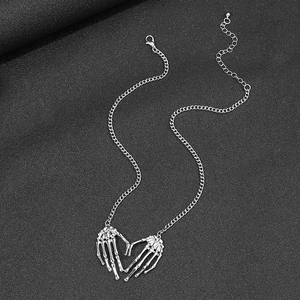 Gothic punk silver skeleton hands heart necklace on a dark textured background