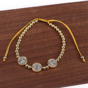 Detailed view of Saint Benedict medals and gold beads on an adjustable cord bracelet