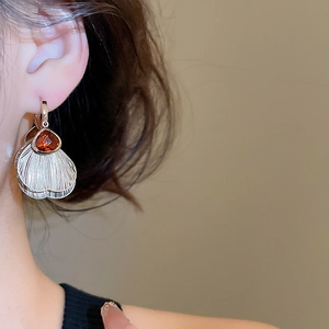 Close-up of model wearing shell-shaped fringe earrings with red gemstone in retro style