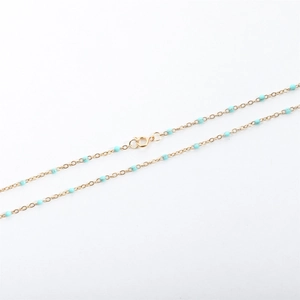 Detail of a gold stainless steel cross chain with turquoise blue enamel beads and spring clasp