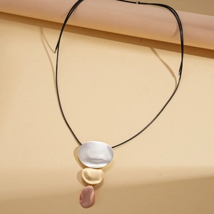 Close-up of three-tone metal oval pendants on a black cord necklace in warm lighting