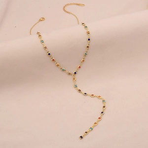 Detailed shot of golden Y-shaped necklace with colorful square crystals on beige fabric