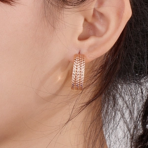 Detail of rose gold C-shaped earrings with wheat-ear texture shown on a model