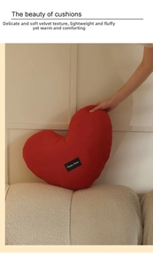 Detail of red heart pillow in plush fabric with Happy Home tag on a beige sofa