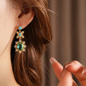 Gros plan de boucles d'oreilles vintage en or avec pierres vert émeraude et turquoise