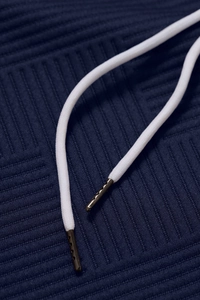 Detail of navy jacquard hoodie fabric with white drawstring and vented metal tips