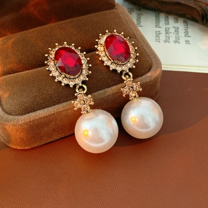 Détail de boucles d'oreilles vintage croix dorée avec gemme rouge et perles