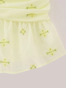 Détail de tissu jaune avec broderie florale verte et motifs géométriques