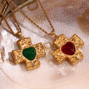 Macro view of gold-plated cross pendants with red and green heart gems on twisted chains