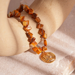 Vintage necklace with brown marble beads and gold coin pendant on stone background