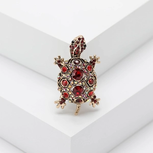 Vintage gold turtle brooch with red and rainbow crystals on a white geometric stand