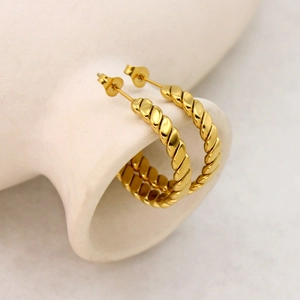 Polished 18K gold plated stainless steel twisted hoop earrings on white ceramic
