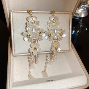 Detail of golden shell flower tassel earrings with pearls in a beige jewelry gift box