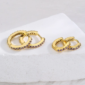 Minimalist gold hoop earrings with purple stone inlays on white stone background