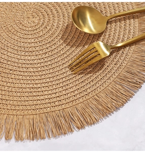 Dettaglio macro di tovaglietta rotonda intrecciata con frange su sfondo marmo