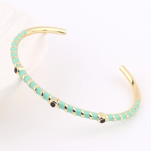 Detail of gold open bangle with mint green enamel stripes and black circular accents