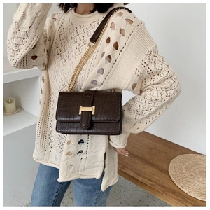 Detail of dark brown crocodile pattern bag with golden H-shaped clasp on a model