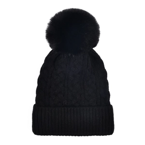 Close-up of black cable-knit beanie featuring a fluffy pompom and thick ribbed cuff