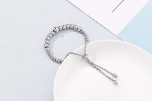 Adjustable silver beaded bracelet with sleek metallic beads on a white porcelain dish