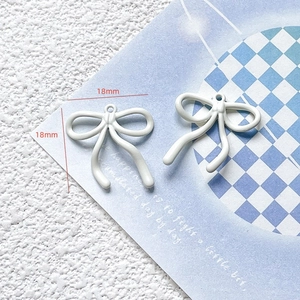 Detailed view of two white 18mm bow charms for DIY jewelry making on a blue grid background