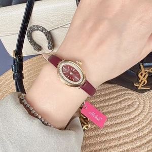 Chic model wearing a gold oval watch with sparkling crystals and a deep burgundy leather strap