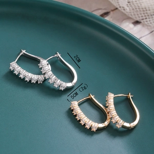 Detail of gold and silver U-shaped earrings with cubic zirconia stones on green ceramic