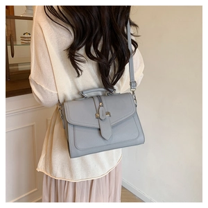 Grey PU leather crossbody bag with metal clasp shown on model in a minimalist room