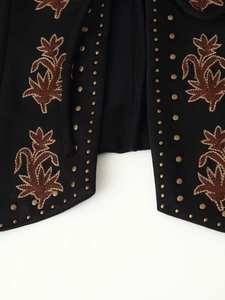 Détail de la broderie ethnique et des clous métalliques sur le gilet en daim noir