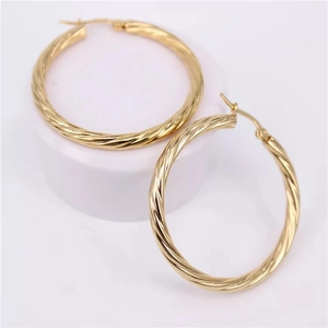 Twisted gold hoop earrings with textured spiral design for women on a white display pedestal