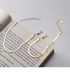 Close-up of gold and silver flat snake bone bracelets resting on an open book
