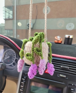 Detail of hand-knitted car charm featuring a beige pot with green leaves and purple fruits