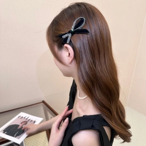 Elegant black bow hair clip with silver rhinestones shown on a model's hair
