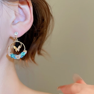 Close-up of gold round earrings with butterfly pendant and blue inlaid gemstones