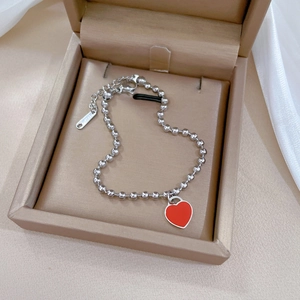 Detailed close-up of a silver beaded bracelet with a red heart pendant in a jewelry box